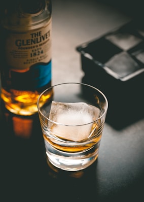 a glass of ice sitting next to a bottle of alcohol