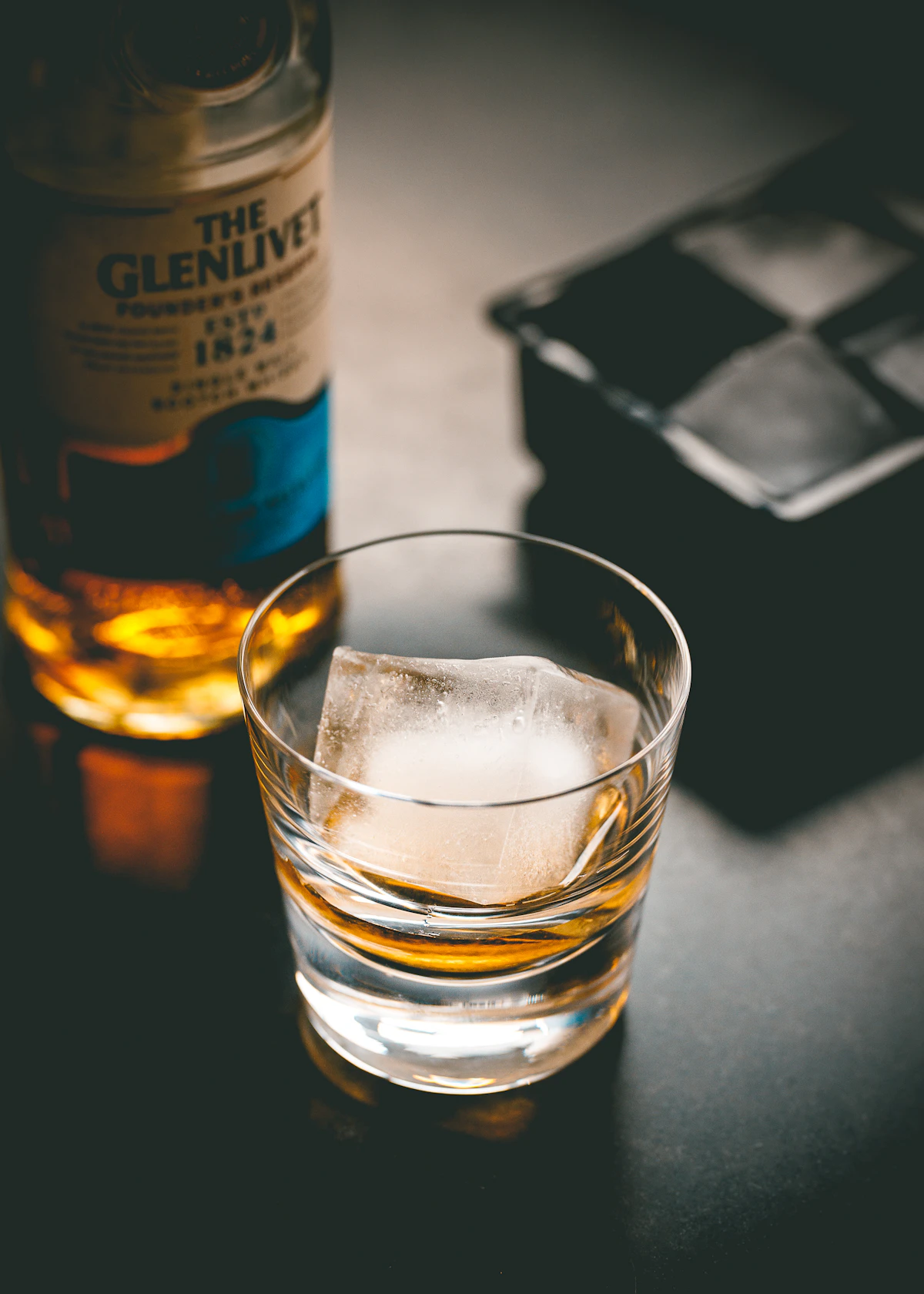 Neat pour of bourbon beside a leather coaster on dark wood.