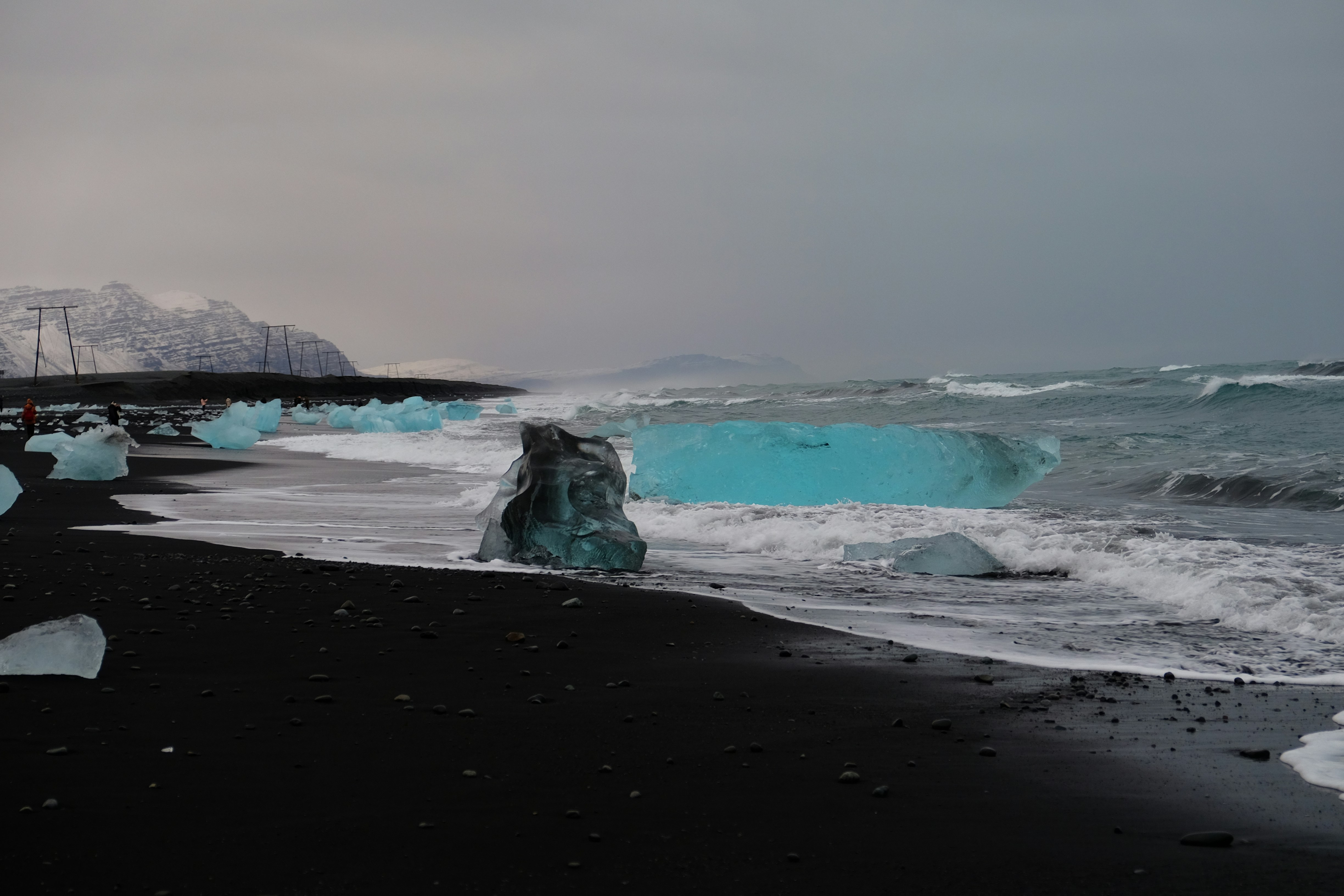 a black beach with icebergs in the water and mountains in the background