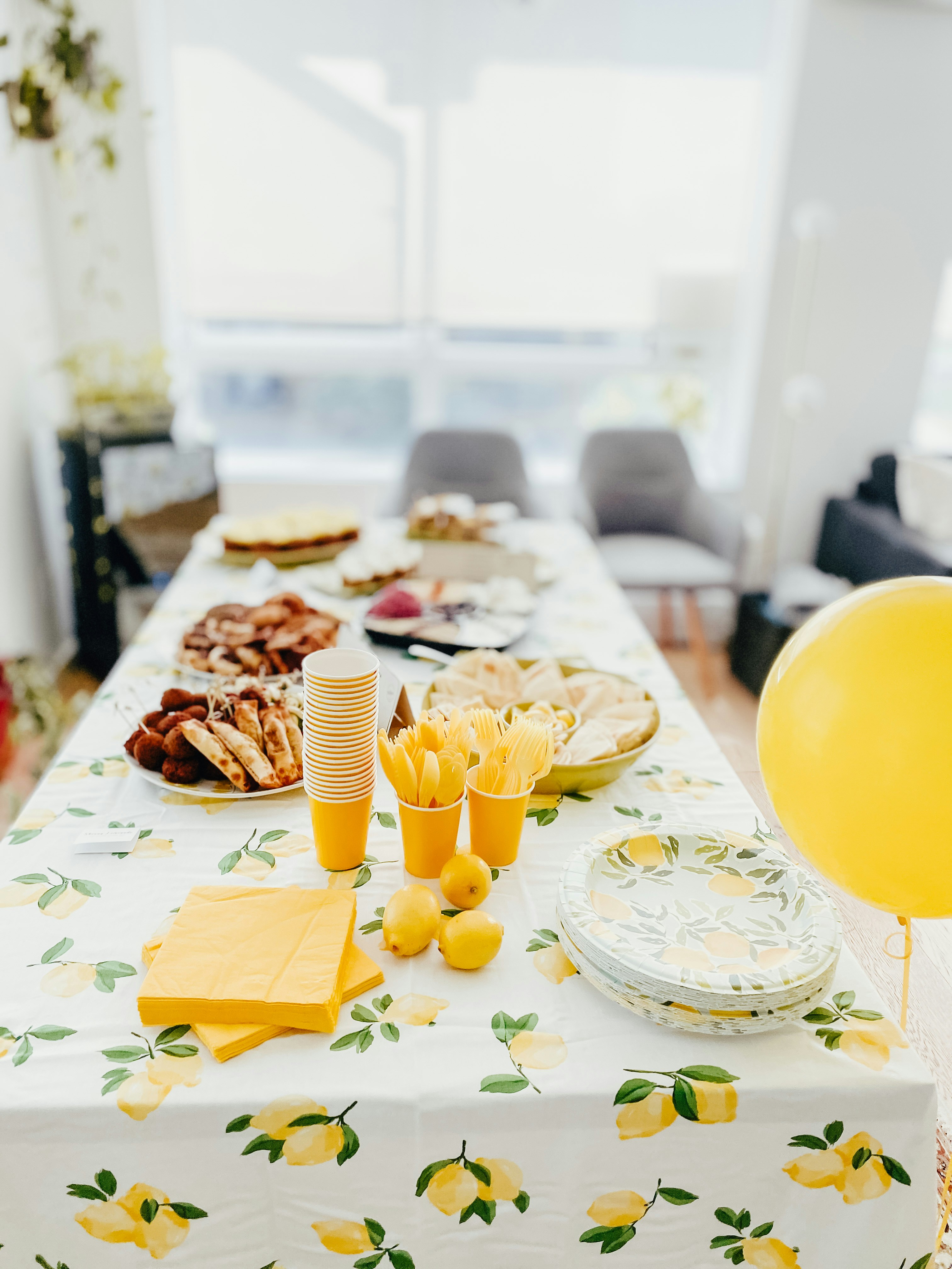 lemon themed party dessert table with yellow decorations and lemon patterned tablecloth