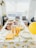 A table is set up for a gathering, adorned with a lemon-themed tablecloth and matching decor. Plates of various finger foods, stacks of disposable cups, and utensils are neatly arranged, along with lemons and a yellow balloon adding a festive touch.