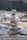 A stack of balanced stones in varying sizes and colors, carefully arranged with a natural backdrop of blurred rocks and greenery. The focus is on the precision of the stone arrangement, which gives a sense of balance and tranquility.