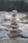 A stack of balanced stones in varying sizes and colors, carefully arranged with a natural backdrop of blurred rocks and greenery. The focus is on the precision of the stone arrangement, which gives a sense of balance and tranquility.