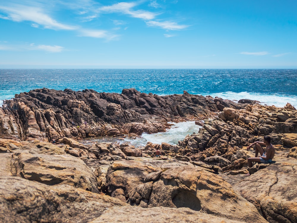 a person sitting on a rock near the ocean