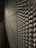 A metallic surface with a complex, repeating textured pattern that creates an optical illusion effect under low-light conditions. The surface features a series of protrusions casting shadows, adding depth to the structure.
