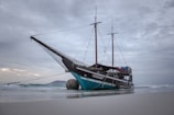 A large wooden pirate ship with black and red sails sailing on turquoise Mediterranean waters under sunny skies