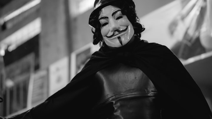 An image of a person wearing an anonymous mask with a black bucket hat and cape