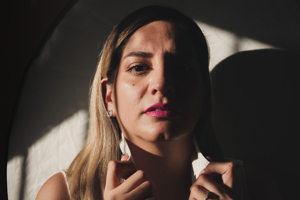 a woman in a white shirt is holding her hand up to her face