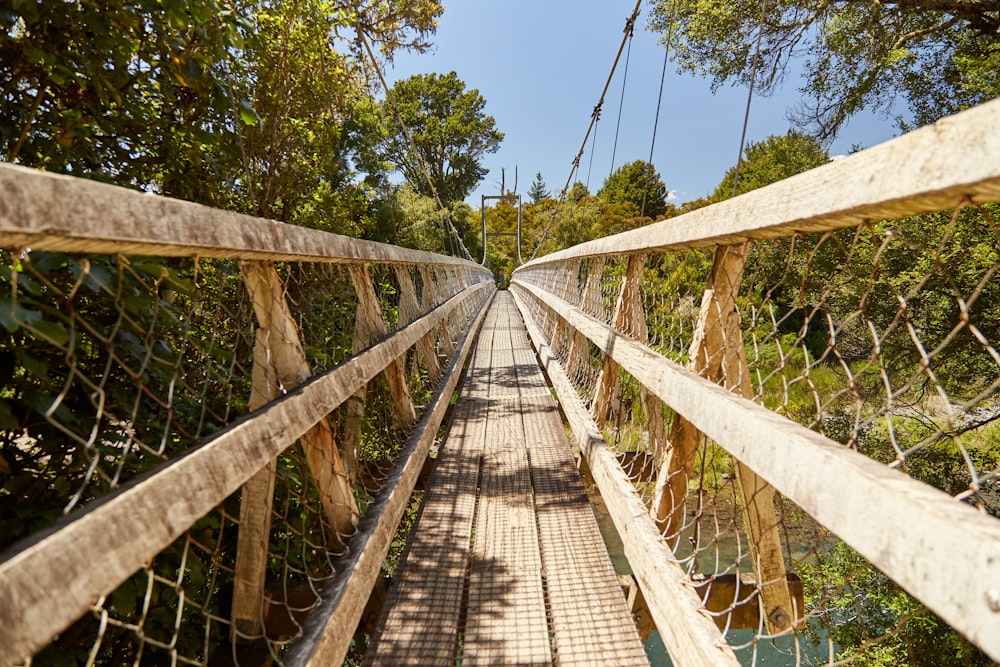 uma ponte suspensa de madeira sobre um rio cercado por árvores