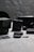 A collection of camera equipment including action cameras, battery packs, and memory cards is arranged on a grey textured surface. The foreground features a prominent action camera and memory card, with additional equipment blurred in the background.