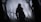 A lone knight in dark, heavy armor stands in a misty, eerie forest gripping a long sword. The atmosphere is somber, with leafless trees surrounding the figure and obscured by thick fog.