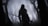 A lone knight in dark, heavy armor stands in a misty, eerie forest gripping a long sword. The atmosphere is somber, with leafless trees surrounding the figure and obscured by thick fog.