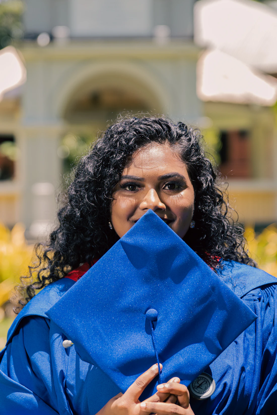 Smiling graduate in a blue gown holding her graduation cap