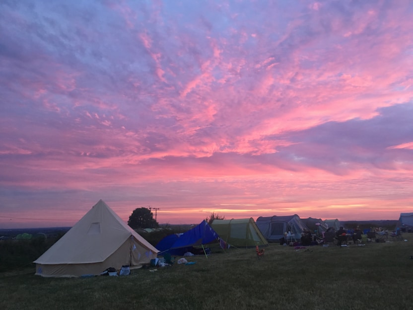 A vibrant outdoor campsite scene with tents, camping gear, and a sunset backdrop