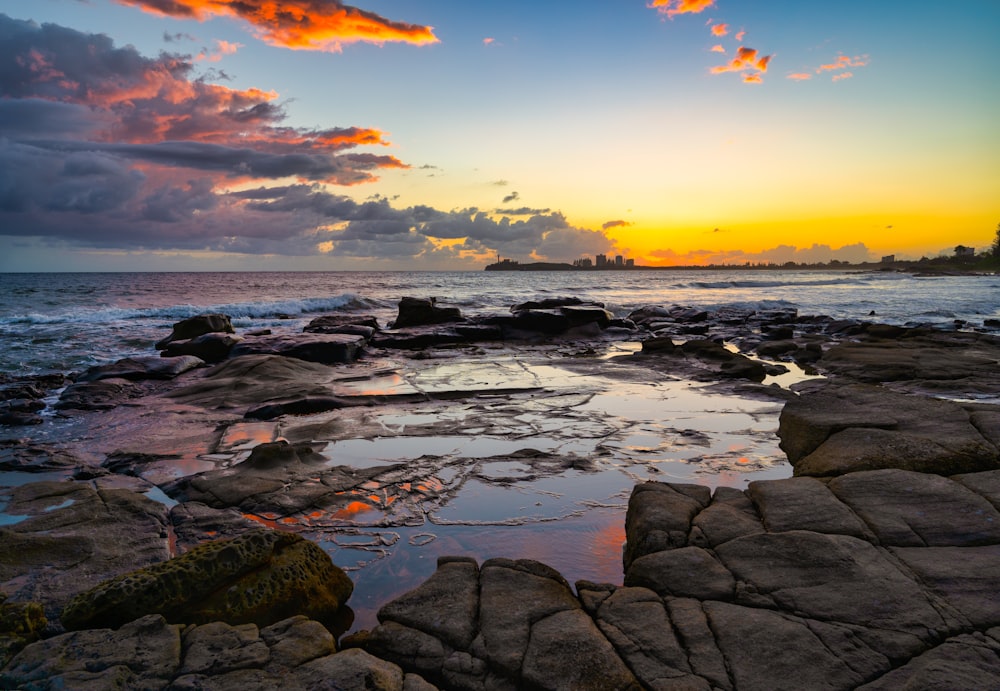 the sun is setting over the ocean and rocks