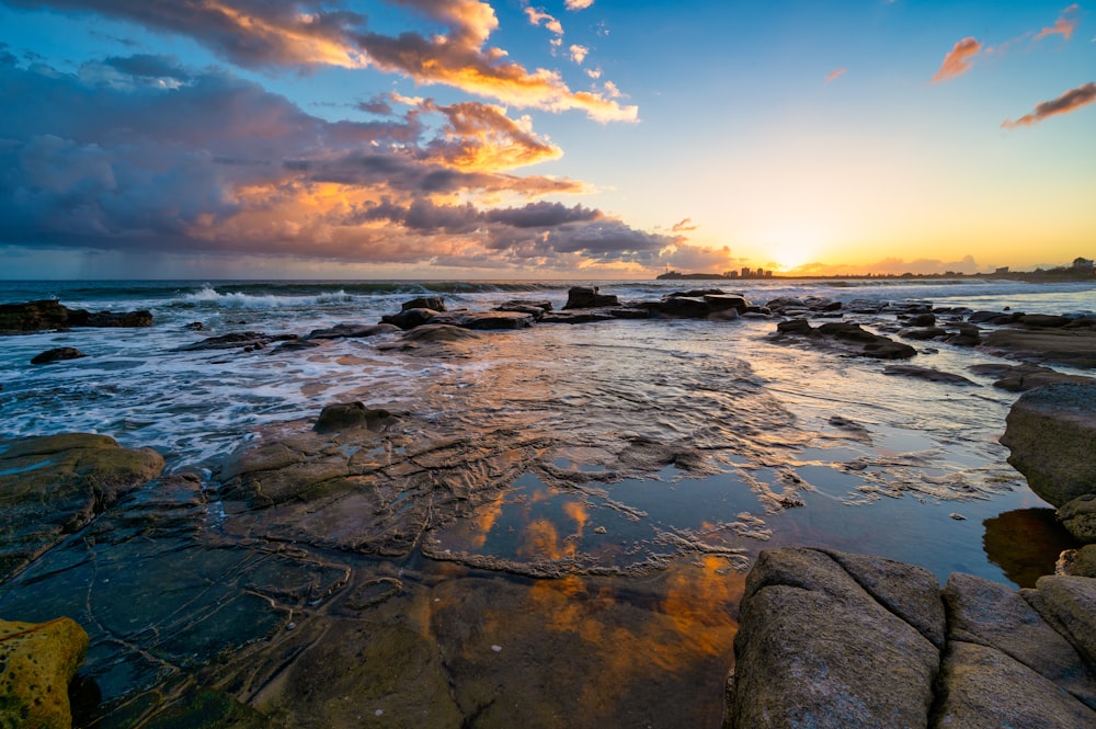 the sun is setting over a rocky beach