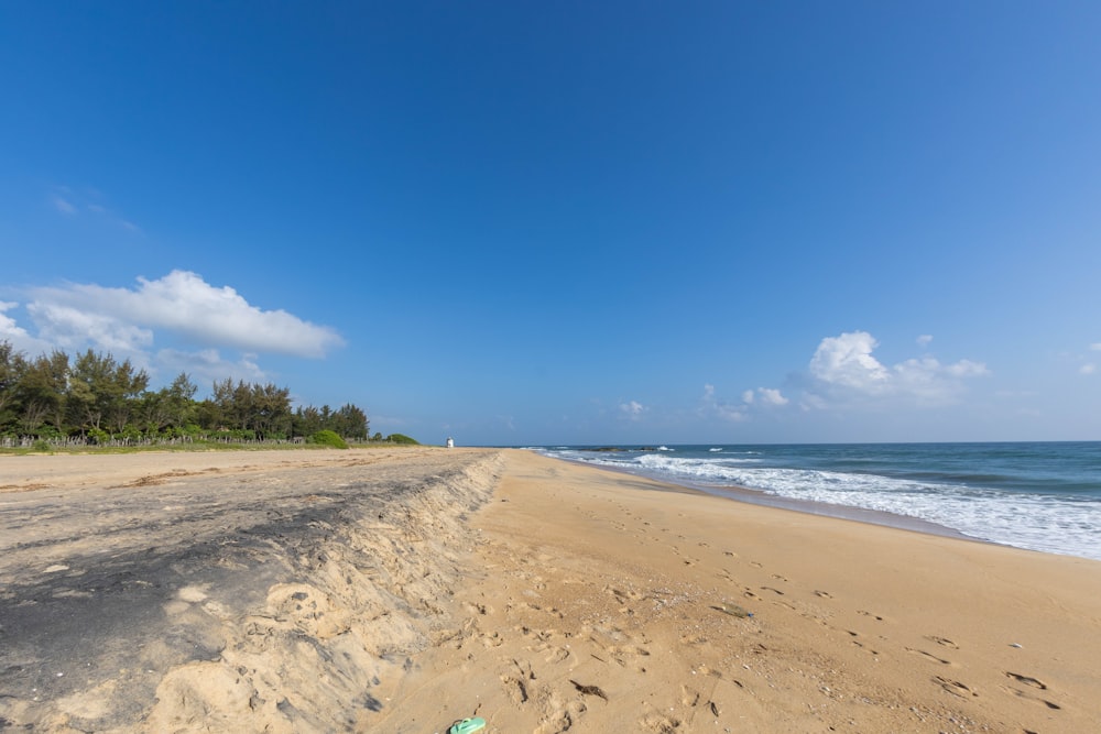 a sandy beach next to the ocean under a blue sky