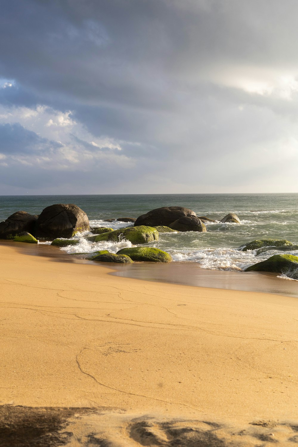 a sandy beach next to the ocean under a cloudy sky