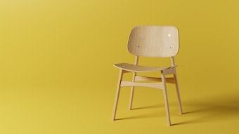 A minimalist wooden chair with a curved backrest and seat is positioned against a solid yellow background. The chair features simple, clean lines and a natural wood finish, contributing to a modern aesthetic.