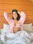 Smiling woman wearing a deep peacock green nightie, sitting relaxed on a cozy bed.