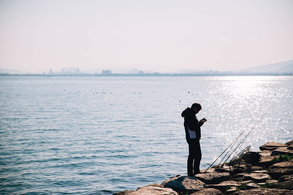 a woman standing on a rock wall next to a body of water