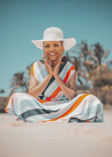 a woman in a white hat is sitting on the beach