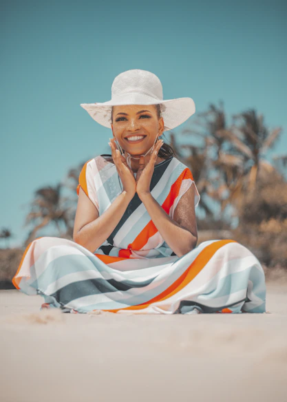 a woman in a white hat is sitting on the beach