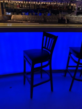 A dimly lit Tokyo bar with empty chairs and a shadowy figure at the counter.