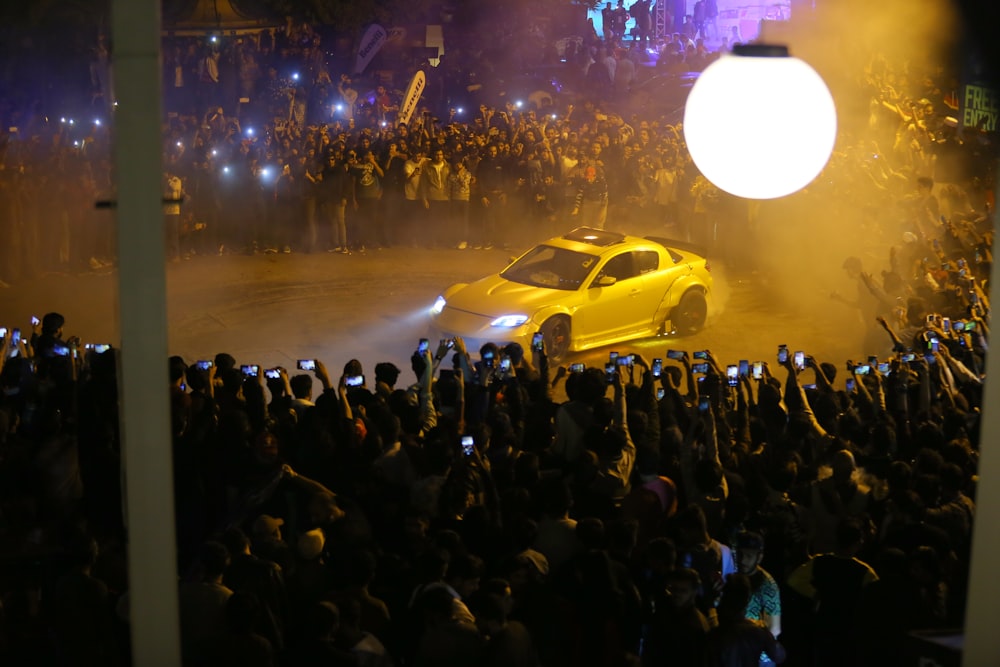 a yellow car driving through a crowd of people