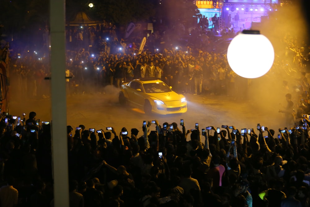 a yellow car driving down a street next to a crowd of people