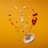 A selection of assorted nuts, fruits, seeds, and spices are artistically arranged in midair against an orange background. The word 'PALEO' is spelled out using letter tiles, surrounded by vibrant pieces of red bell pepper, carrot slices, and a scattering of seeds. A small white bowl lies below, filled with a mix of nuts being poured out.
