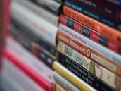 A stack of books with various titles is shown, featuring religious and spiritual themes. The spines are vertically aligned, showcasing different fonts and colors. Some titles include words like 'God' and 'Devotional,' suggesting content related to theology or religious studies. The image is focused on the books in the foreground, with the background slightly blurred.