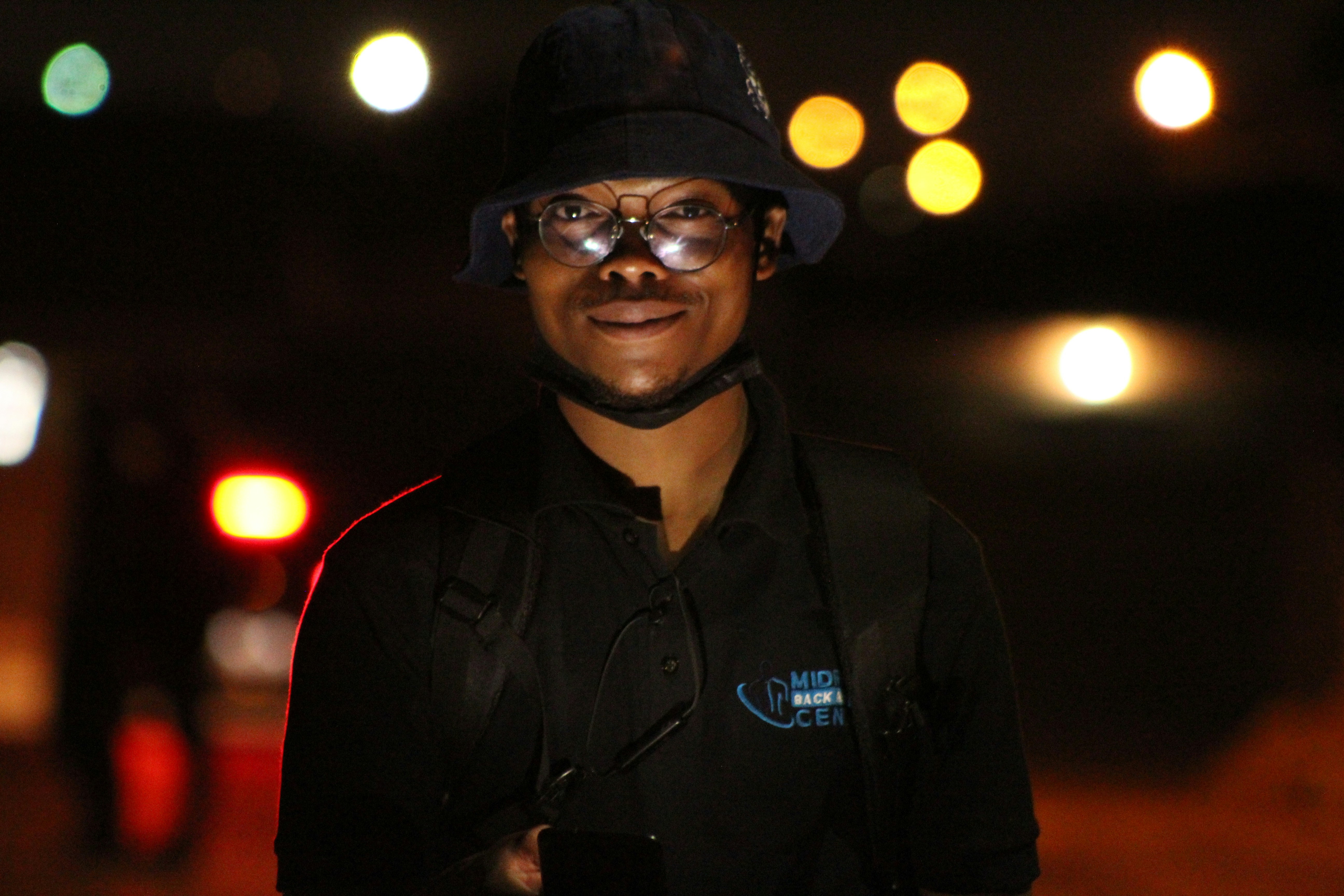 a man wearing a hat and glasses standing in the dark
