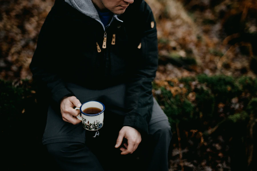 A man cradling an enamel mug of tea outdoors, thoughtful expression, lived-in clothes