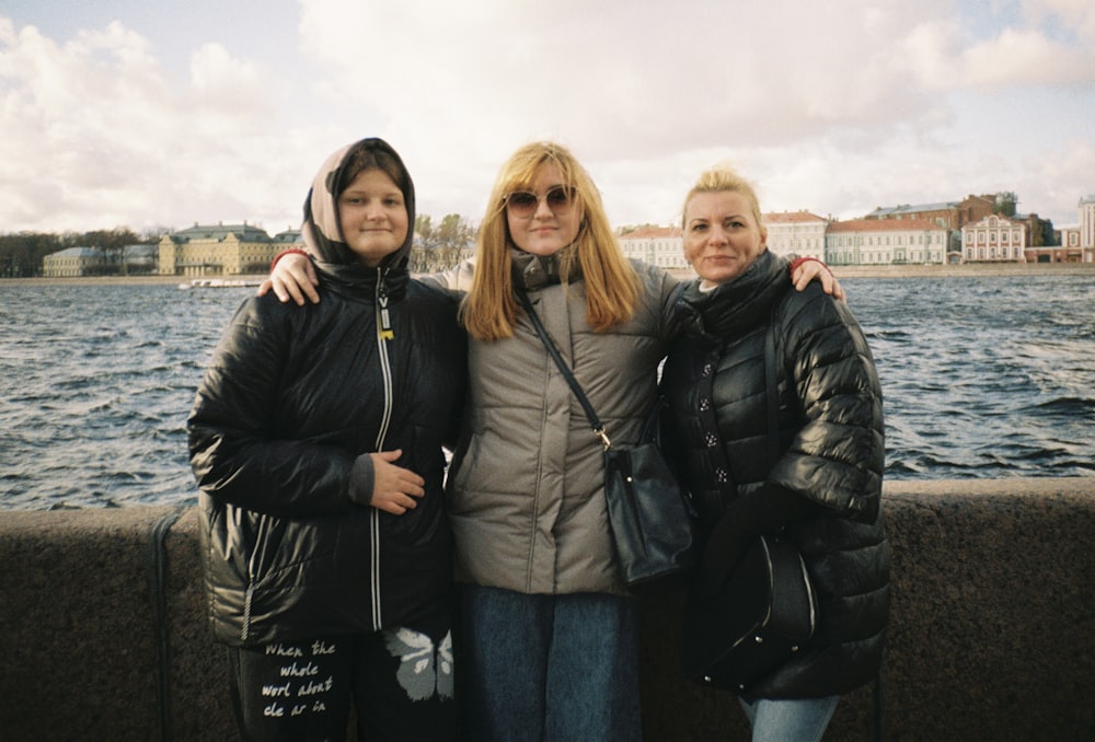 three women standing next to each other near a body of water