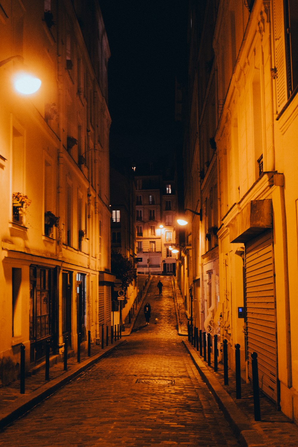 a narrow street at night with a person walking down it