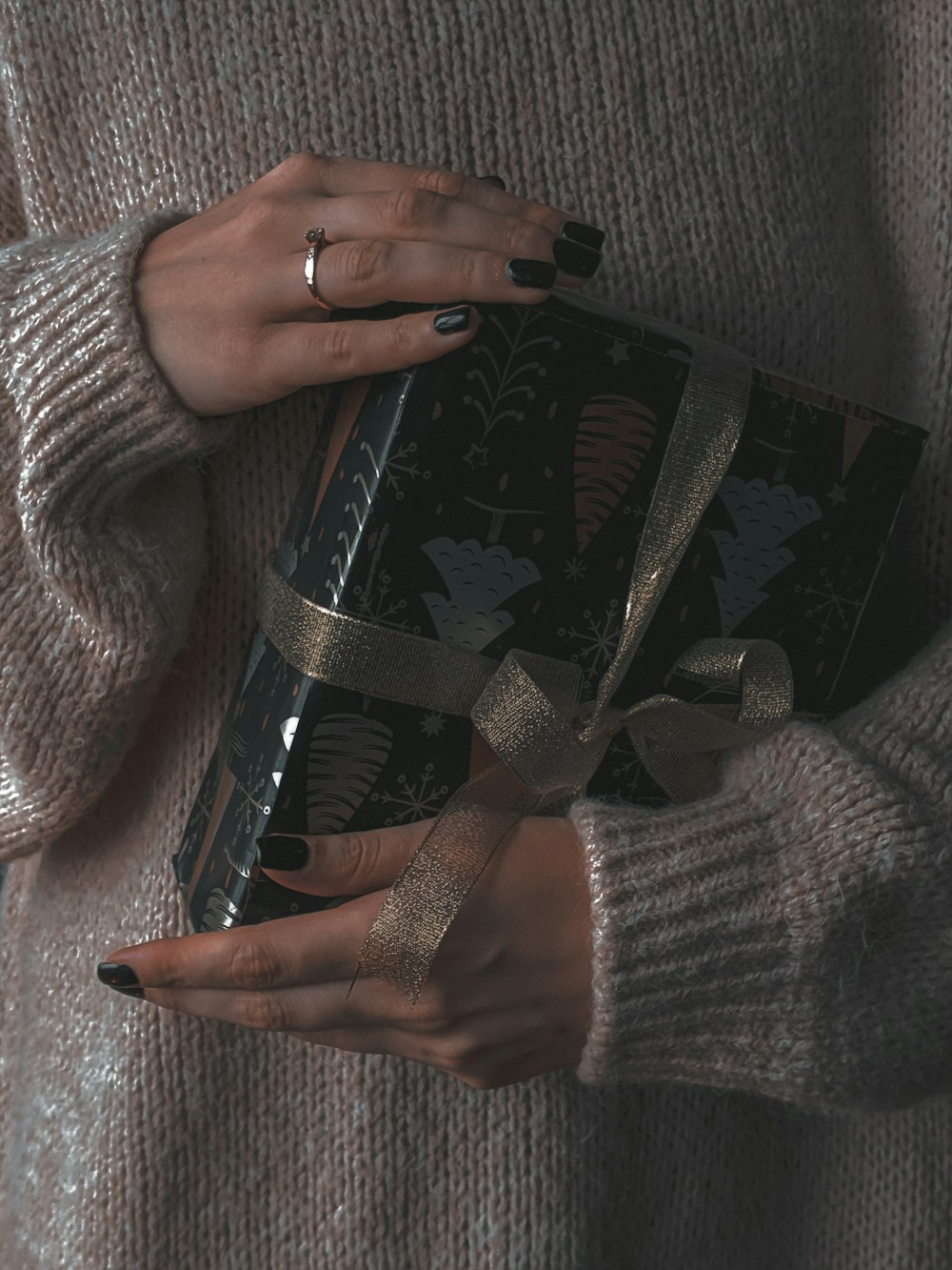 a woman holding a black gift box with a gold ribbon