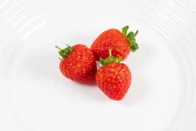three strawberries sitting on a white plate