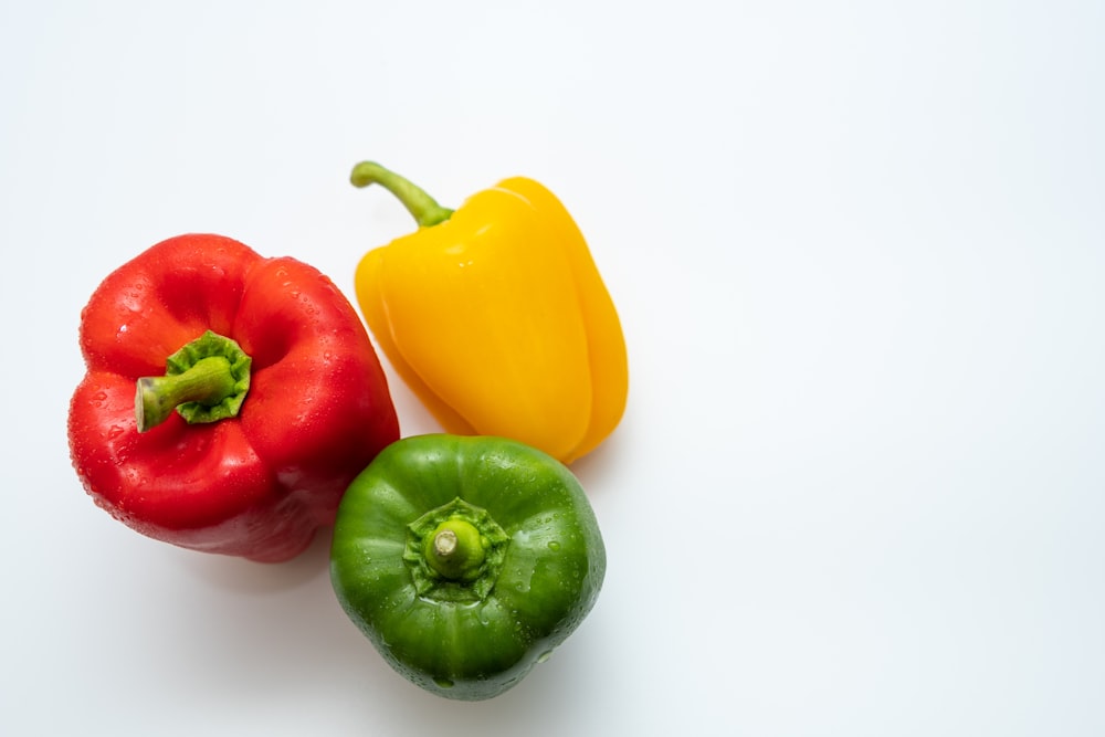 three different colored peppers on a white surface