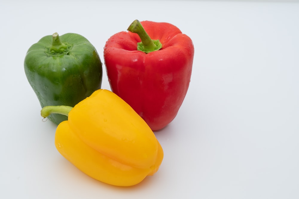 three different colored peppers on a white surface