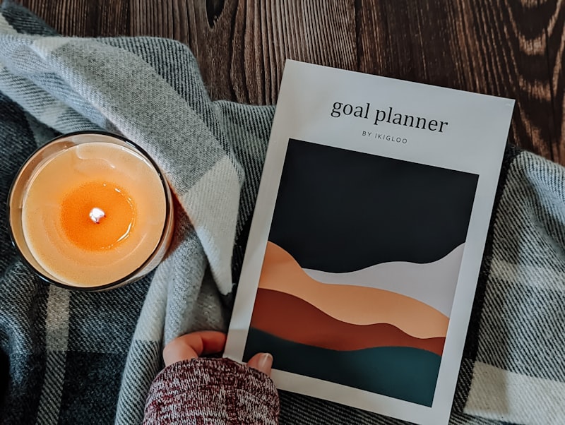 A person holding a planner beside a lit candle on a textured blanket
