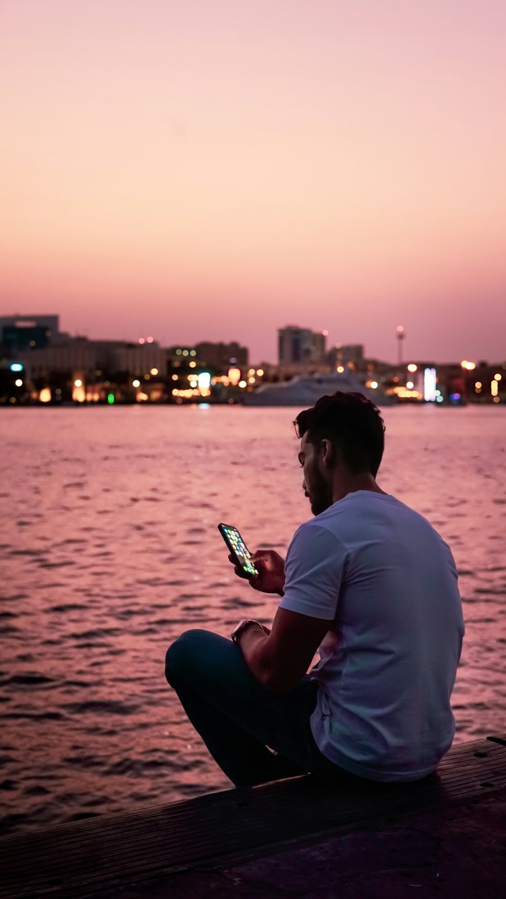 a man sitting on a dock looking at his cell phone