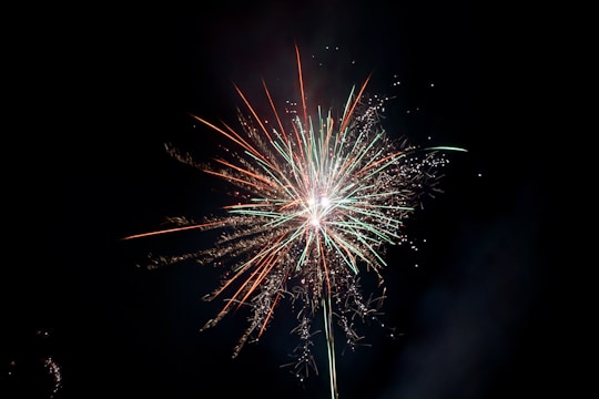 Bright fireworks with green and red streaks burst against a dark night sky, creating a vivid display of color and light.