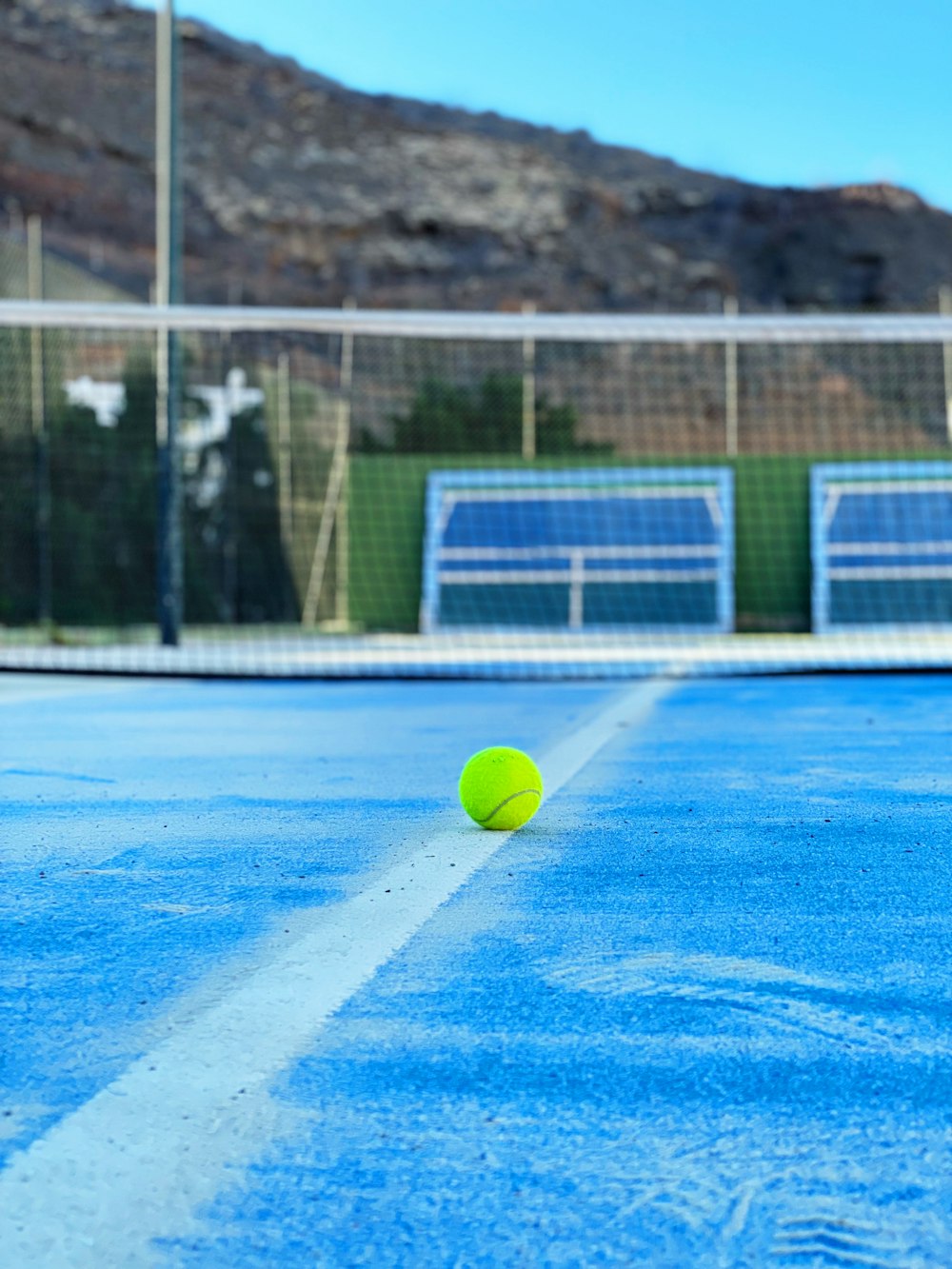 Una pelota de tenis en una cancha de tenis con montañas al fondo