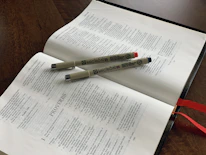 Close-up of an open Bible with a gold pen resting on cream-colored pages.