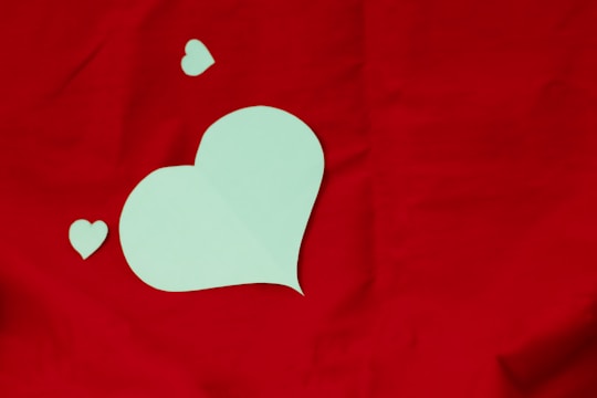 A large, light green heart cutout is placed on a vibrant red background. Two smaller heart cutouts are positioned nearby, creating a playful and romantic arrangement.