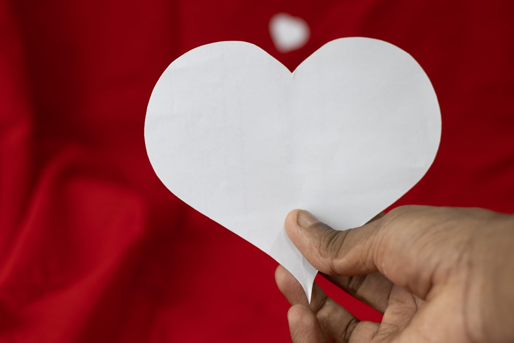 a person holding a paper heart in front of a red background