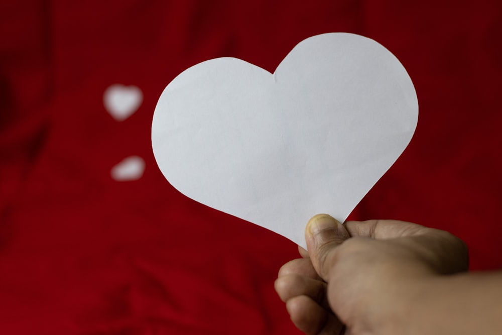 a person holding a paper heart in front of a red background