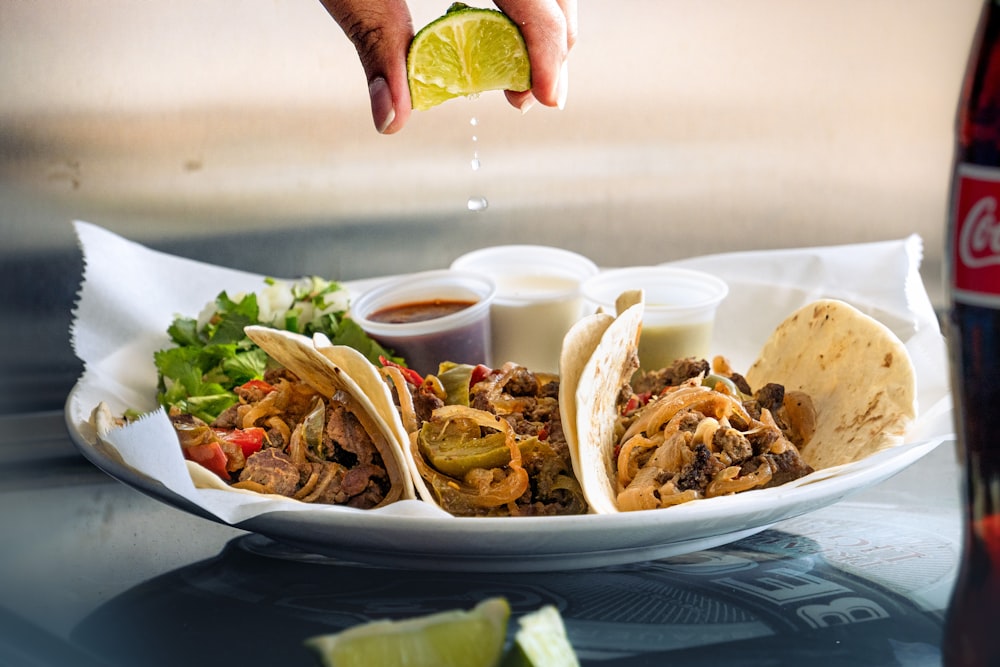 a plate of tacos with a lime being drizzled on top