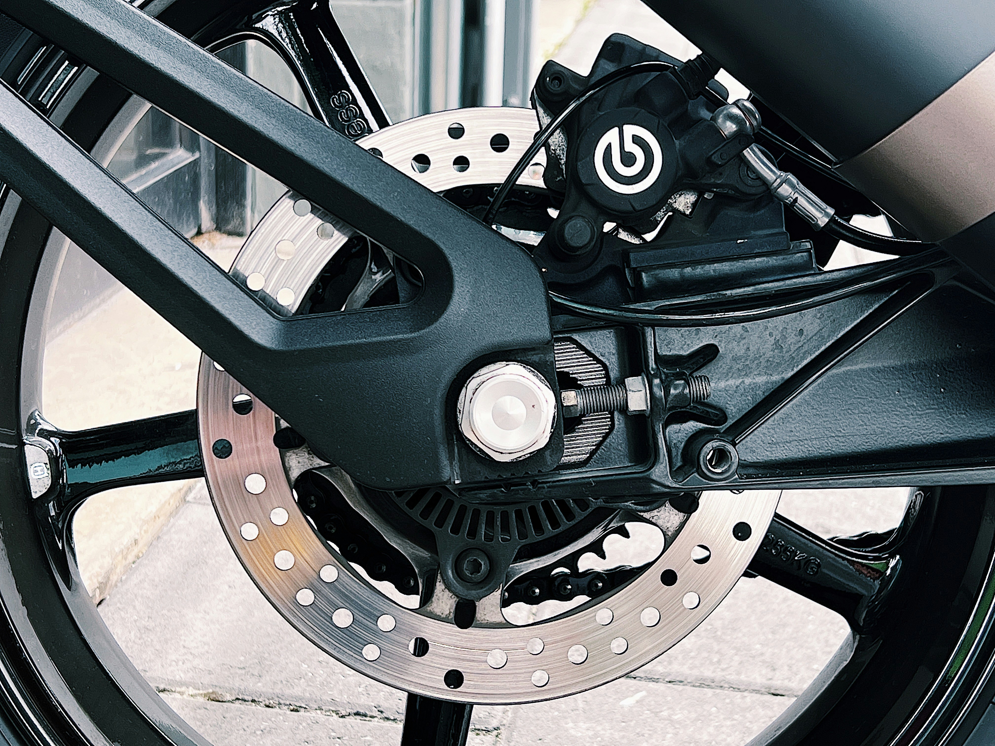 Close-up of motorcycle brake caliper with braided line and drilled rotor.